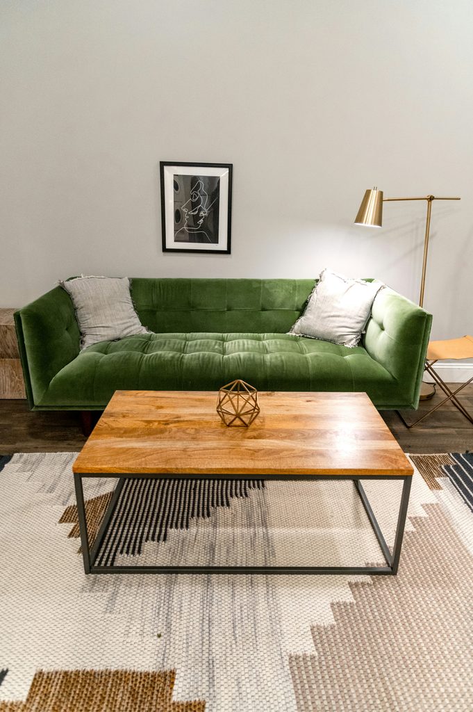 Zielona aksamitna sofa z jasnym dywanem o geometrycznym wzorze w salonie.